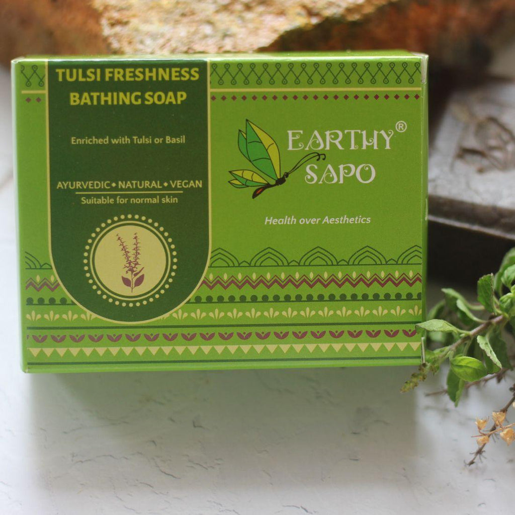 Earthy Sapo Tulsi Freshness Bathing Soap packaging displayed with fresh tulsi leaves.