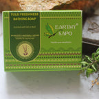 Earthy Sapo Tulsi Freshness Bathing Soap packaging displayed with fresh tulsi leaves.
